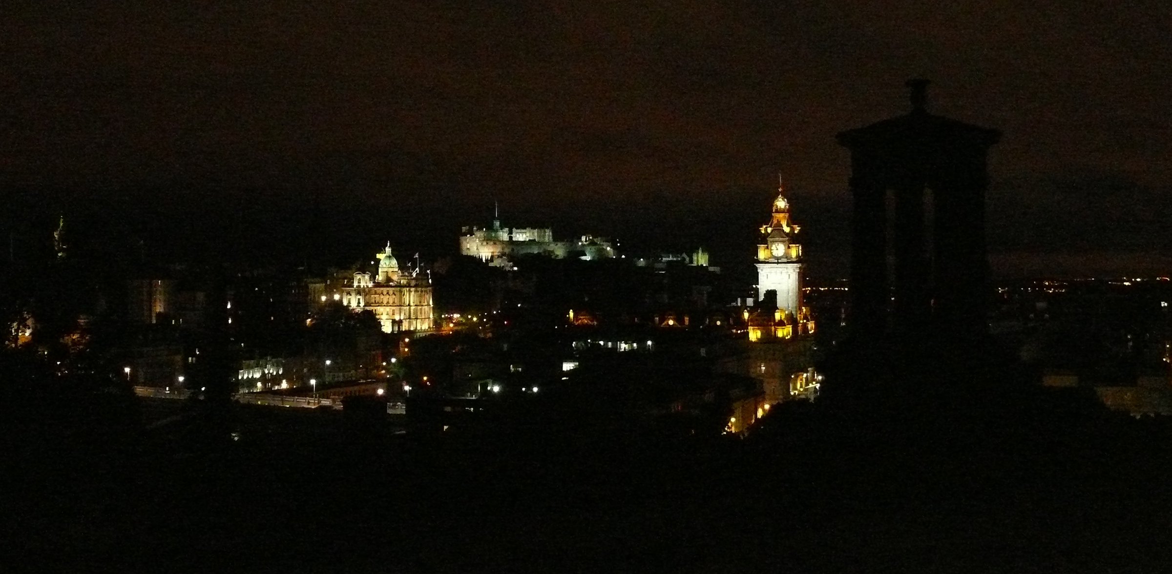 View of Edinburgh at night from Calton Hill, with the silhouette of the Dugald Stewart Monument visible.